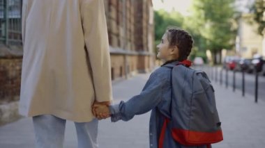 Arkadan bak. Kapatın. Annesinin elini tutan mutlu okul kızının portresi. Kadın ebeveyn ve çocuk sokakta otuzbir çekiyor. Konuşuyor ve gülümsüyor. Aile ilişkisi kavramı