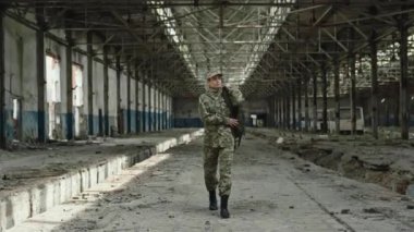 Mahvolmuş fabrikada yürürken sırtında teçhizatla sırt çantası taşıyan beyaz, kendine güvenen bir kadın. Görevden ayrılan cesur kadın asker..