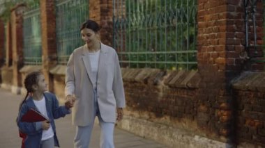 Anne ve kızı okuldan sonra eve yürürken konuşuyor ve gülümsüyor. Yetişkin bir kadın çocuğun elini tutuyor ve okuldaki günü soruyor. Eğitim ve çocuk bakımı kavramı