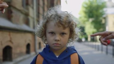 Adults bullying schoolboy with a backpack on the street near school. Sad kid looking at camera. Close up of face of upset abused kid. Violence and bullying concept