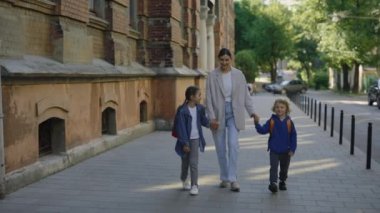 Küçük çocukların okulda ilk günü. Anne oğluna ve kızına okula kadar eşlik edecek. Ebeveynler el ele tutuşup sokakta çocuklarla konuşuyor. Mutlu aile kavramı