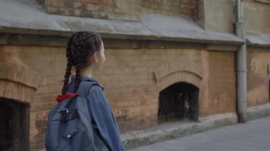 Okulun yakınındaki sokakta kot ceketli küçük bir kızın arka görüntüsü. Çocuk okuldan dönüyor. Eğitim ve mutlu çocukluk kavramı