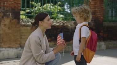 Anne çocuğuna bakıp Amerikan bayrağı veren oğluyla konuşuyor. Küçük gülümseyen vatansever çocuk yetişkin kadınlara bakıyor ve ABD bayrağını alıyor. Eğitim ve vatanseverlik kavramı
