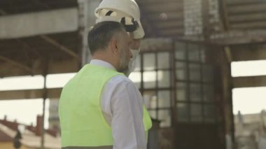 Çalışma alanındaki inşaat sırasında koruyucu başlık takan beyaz bir adamın arka görüntüsü. Güvenlik üniforması ve kaza önleme kavramı.