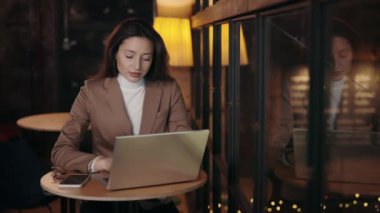 Charming young woman dressed in stylish formal jacket using modern laptop for remote work while sitting at cafe table. Business lady with solving urgent issues online.