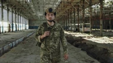 Gizli askeri görev sırasında terk edilmiş çelik fabrikasında yürüyen koruyucu kasklı ve kamuflaj üniformalı kendine güvenen beyaz bir adam. Halk, güvenlik ve savunma kavramı.