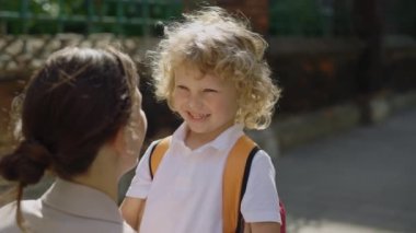 Mother asking her son about his first day at school. Curly little child standing near his mom and hug her. Back to school concept. Close up