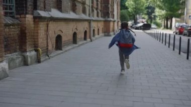 Happy little girl with backpack and notes is running to school. Schoolgirl is running to class room at schoolyard. Education and people concept. Back view
