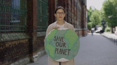 Single female eco activist standing and holding banner save our planet on street. Young teacher looking at camera protest against environmental pollution, save Earth. Eco concept