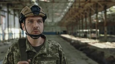 Brave caucasian man in safety helmet and military uniform looking around while walking on destroyed industrial manufacture. Qualified officer on secret military mission.