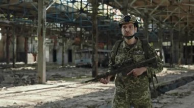 Armed brave man in military US uniform walking among destroyed industrial plant with real gun in hands. Military mission and defence concept.