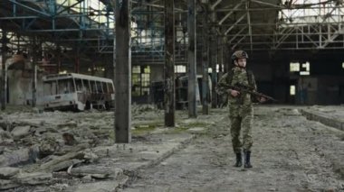 Military female soldier in camouflage uniform holding automatic rifle while patrolling territory in ruined factory. Concept of people, infantry and mission.