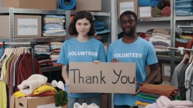 Dolap afişi taşıyan çeşitli erkek gönüllülerin portre görüntüsü teşekkür cümlesiyle ve gülümseyerek kameraya bakıyor. Arkasında eşyalar olan raflar. İnsani yardım kavramı