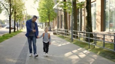Back to school. Little child with bag holding hand in hand his father. Male person taking his son to school. Concept of education and family