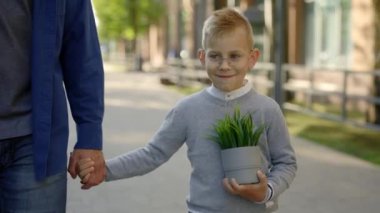 Close view of the father holding sons hand and son is holding the plant in a pot after ecology lesson at school smiling wearing glasses. People, education and ecological concept