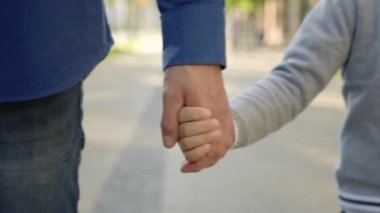 Close view of the father and sons hands. Father holds his son hands after school while going home. Father-son relationship and people concept