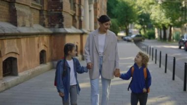 Küçük çocukların okulda ilk günü. Anne oğluna ve kızına okula kadar eşlik edecek. Ebeveynler el ele tutuşup sokakta çocuklarla konuşuyor. Mutlu aile kavramı