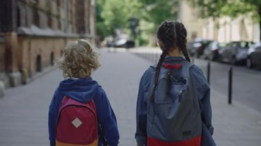 Little boy and girl with backpacks go to school. Classmates walking and talking on the street. Back view. Back to school, knowledge day. Education concept