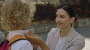 Mother carry about her child. Mommy correct collar on shirt of son stroking child near school classes embraces hugs cuddles hispanic school boy hugging mum outdoors. Education and family concept