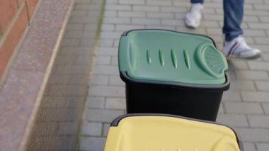 Close view of the sorting bin and the male hands in gloves puts two glass bottles inside the glass sorting bin. Volunteer is sorting the glass bottles into the bins