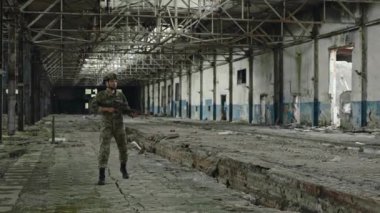 Concentrated soldier in special forces uniform walking through abandoned building after successful mission. Military man with devastating weapon looking around.