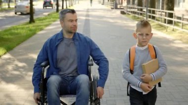 A disabled father veteran in a wheelchair and his son talk about school and how he spent his day after school son is wearing glasses and holding book from school library