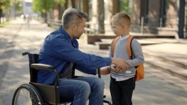 Disable father tells his son a story and takes five with his son on the school yard. Male businessman says goodbye to his son in front of the school. Family and disabled people concept