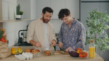 Lgbt family couple standing together in their new apartment in the kitchen and cooking salad, talking to each other. People and relationship concept
