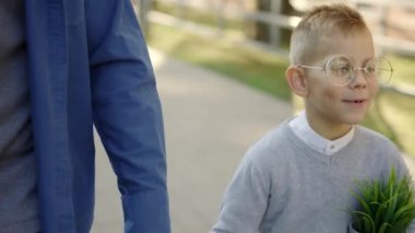 Close view of the father holding sons hand and son is holding the plant in a pot telling father how was his day at school after biology lesson at school smiling wearing glasses