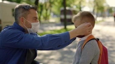 Close up of the disabled father in mask sitting on the wheel chair wearing mask to his son before school because of the pandemic. Pandemic and disabled people concept