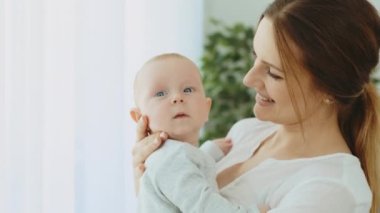 A young mother holds a newborn baby in her arms while the baby looks at the camera. Motherhood concept