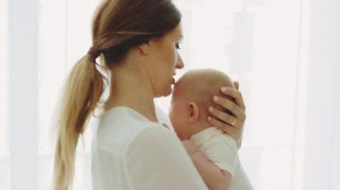 Back view of the caucasian mother holding and swings her newborn baby before sleeping and kissing the head of a baby. Motherhood concept