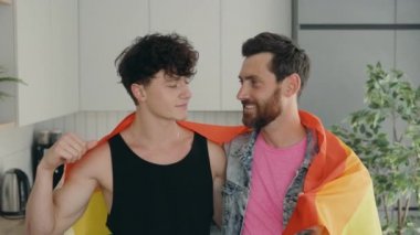 Portrait of handsome man gay family holding lgbt flag and smile. Attractive romantic male lgbt couple standing in their new home in morning and looking at camera with gay pride and rainbow background