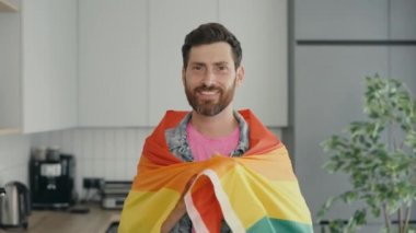 Portrait shot of middle aged smiled gay man wearing rainbow flag over his shoulder and looking at camera while posing. People and lgbt concept