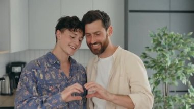 Portrait of the two lgbt men standing in their new apartment and showing heart shape using their arms. People and lgtb concept