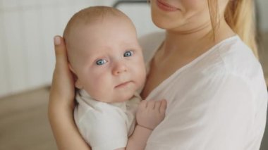 Close view of the newborn baby looking at the camera while his mother holding him. Motherhood concept