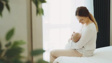 Happy caucasian mother breastfeeding newborn baby sitting on the bed. Concept breast feeding and lactation infant. Baby eating mothers milk. Young woman nursing and feeding baby