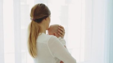 Back view of the caucasian mother holding and swings her newborn baby before sleeping and telling fairy tales for her baby before sleeping. Motherhood concept