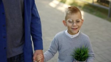 Father holding son hand and child is holding the plant in a pot telling father stories from school after biology lesson smiling wearing glasses. Back to school