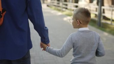 Male person taking his son to school. Father holding son hand and telling father stories from school biology lesson. Focus on boy. Concept of education and family