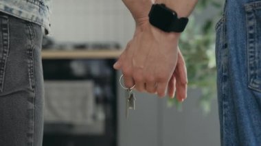 Close up of the gays hands holding keys in their new apartment and one partner wearing smartwatch. Happy couple holding hands together and the key from their new home. Moving and lgbt concept