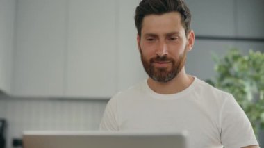 Businessman using computer remote distance working sitting at kitchen table drinking coffee. Caucasian student studying online on laptop at home office. Home office
