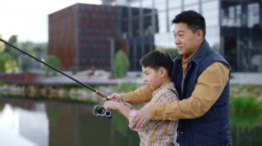 Asian father teach his son how to cast a fishing rod correctly from the pier. Dad and son. Father help his son cast a fishing rod correctly from the pier. Family and fishing concept