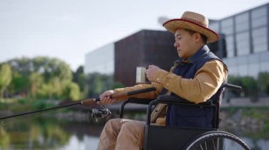 Disabled asian man wearing special fishing clothes fishing in the early morning and drinks hot drink on the pier. Disabled people and fishing concept
