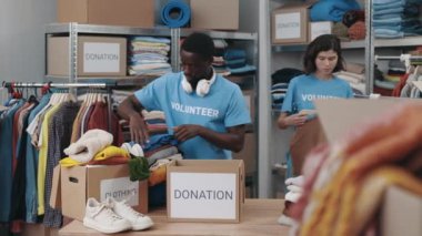 Diverse male and female volunteers sorting clothes and putting it into the cupboard box at the donation center. Humanitarian aid and donating concept