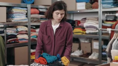 Caucasian brunette female putting box with clothes for recycle or donating and wokring with laptop at the charity shop. Reuse, second-hand, conscious consumer, sustainability concept