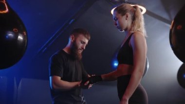 Male trainer is helping woman with the hand bandage on the boxing gym background before the hard training. Training day with coach in the boxing gym