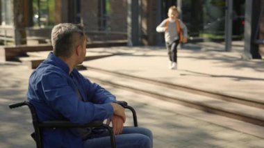 Close view of the disabled father waiting his son from the school. Happy boy running from the school to take five his disabled father. Family and disabled people concept