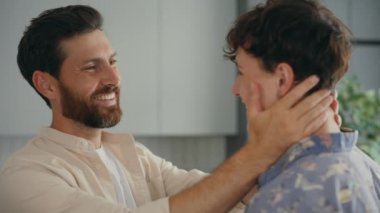 Close up view of the one lgbt partner holding the head of another partner and they happily talking and smiling to each other standing in the kitchen. People and relationship concept