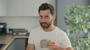 Portrait of the happy smiled middle aged man worker sitting in their new apartments in the kitchen drinking hor tea or coffee. People and leisure time concept
